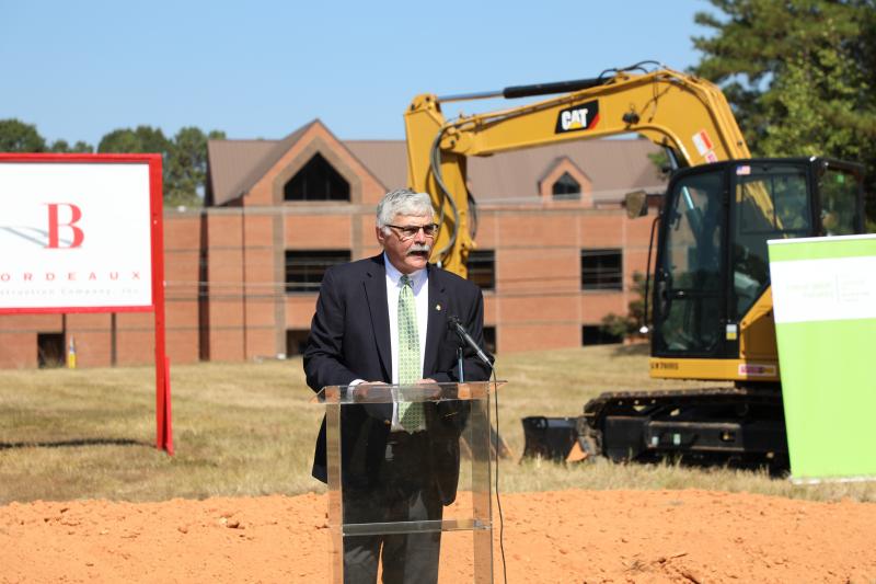 dr. ingram standing behind podium at groundbreaking ceremony, with construction equipment and dirt behind him