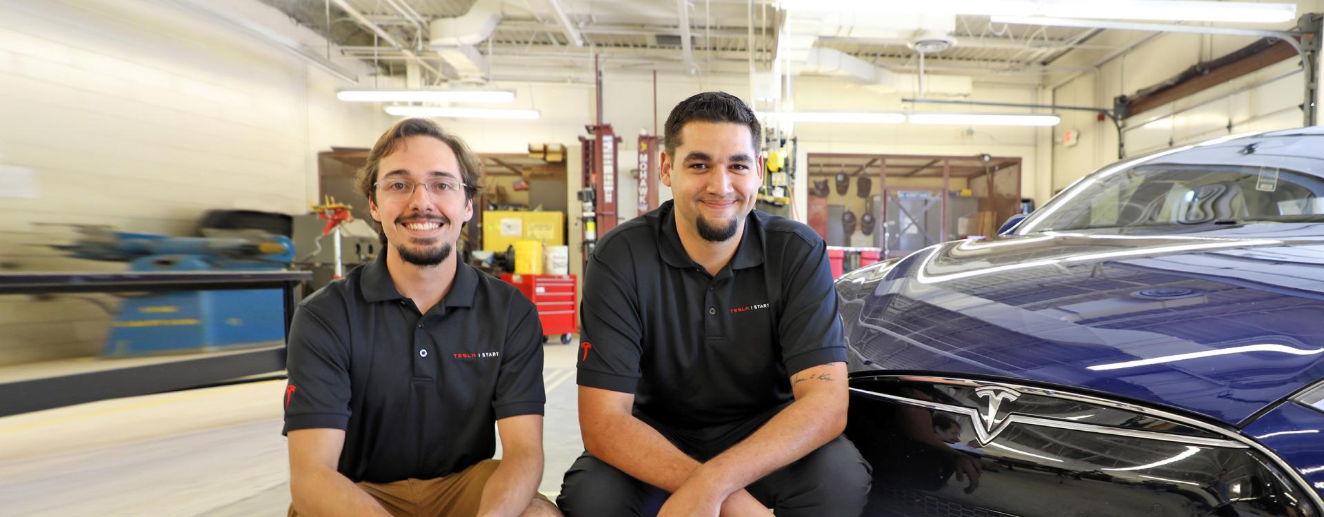 two automotive students on internship sitting next to Tesla car 