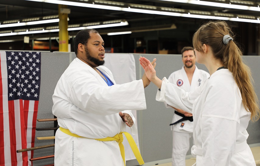 two students practice aikido ove, raising arms, crossed, while instructor looks on