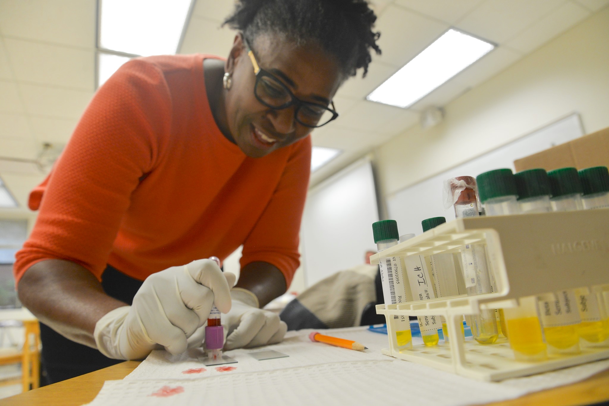 student wearing gloves leaning over desk recording blood sample in little tubes