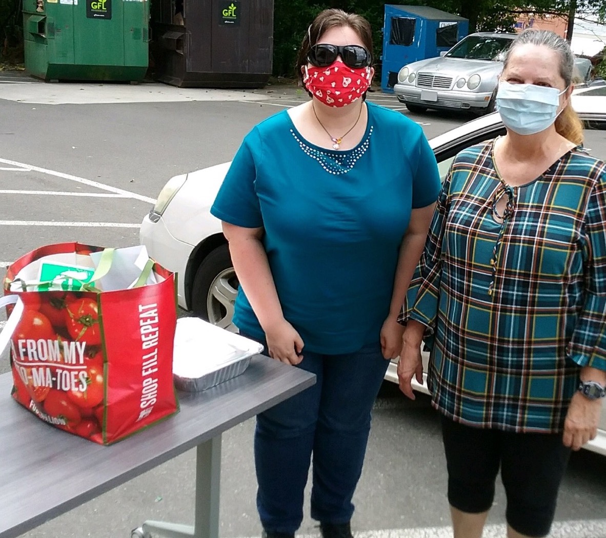 two students with face masks standing next to their bag of groceries