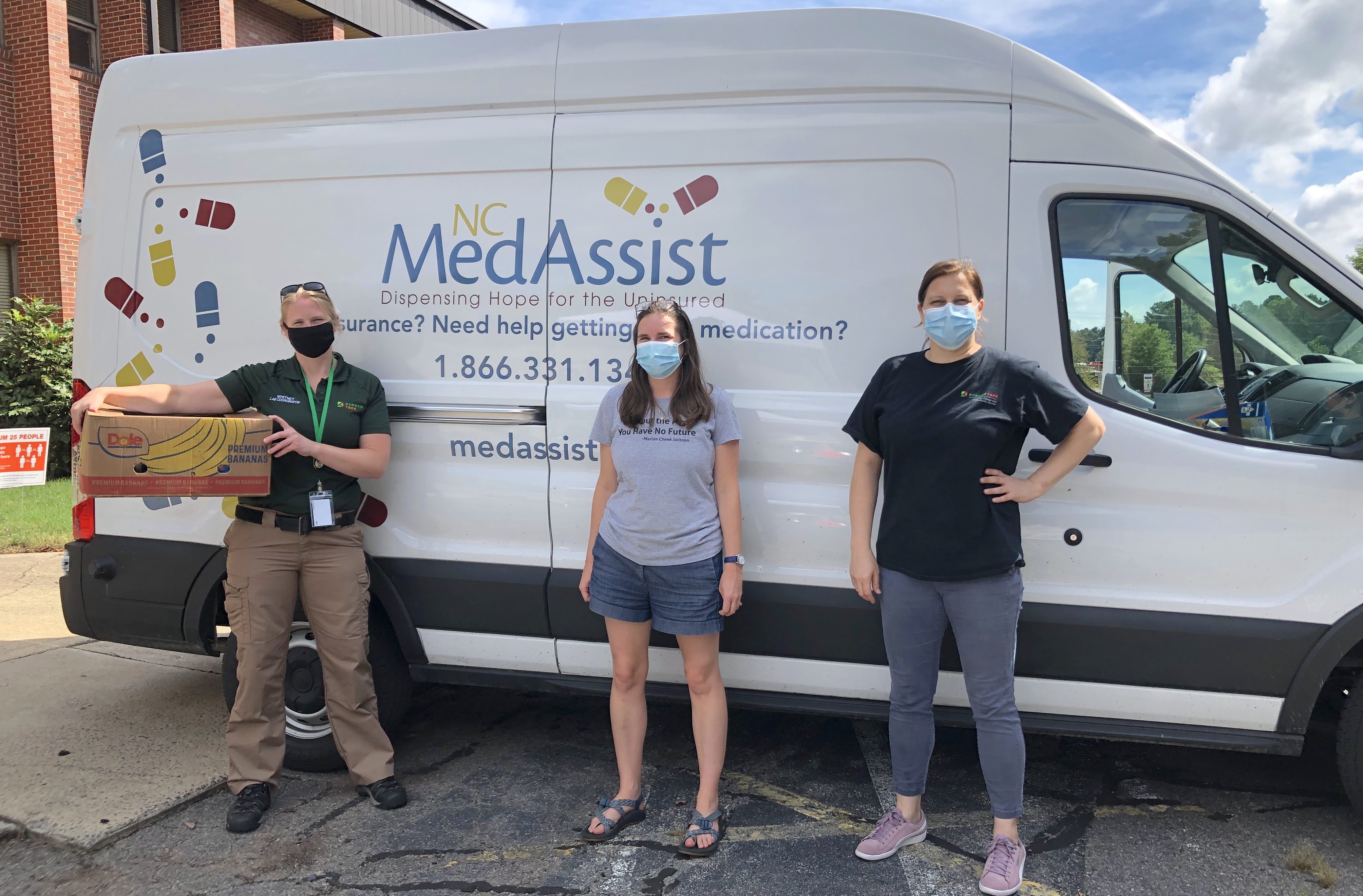 three people standing in front of medassist truck smiling and wearing masks