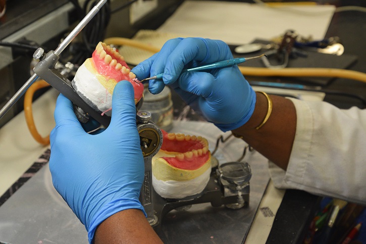 close up of hands wearing blue gloves and holding fake teeth using dental equipment