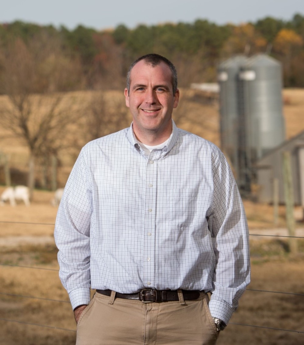 Derek Foster posing in front of a livestock farm