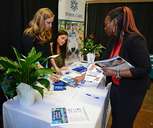 student collects Nurse Care information at a table at a job fair