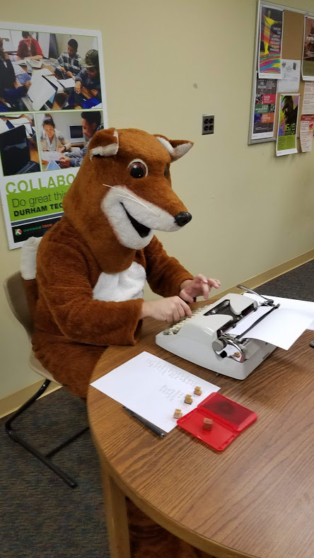 The Poetry Fox sitting at a table with a typewriter.