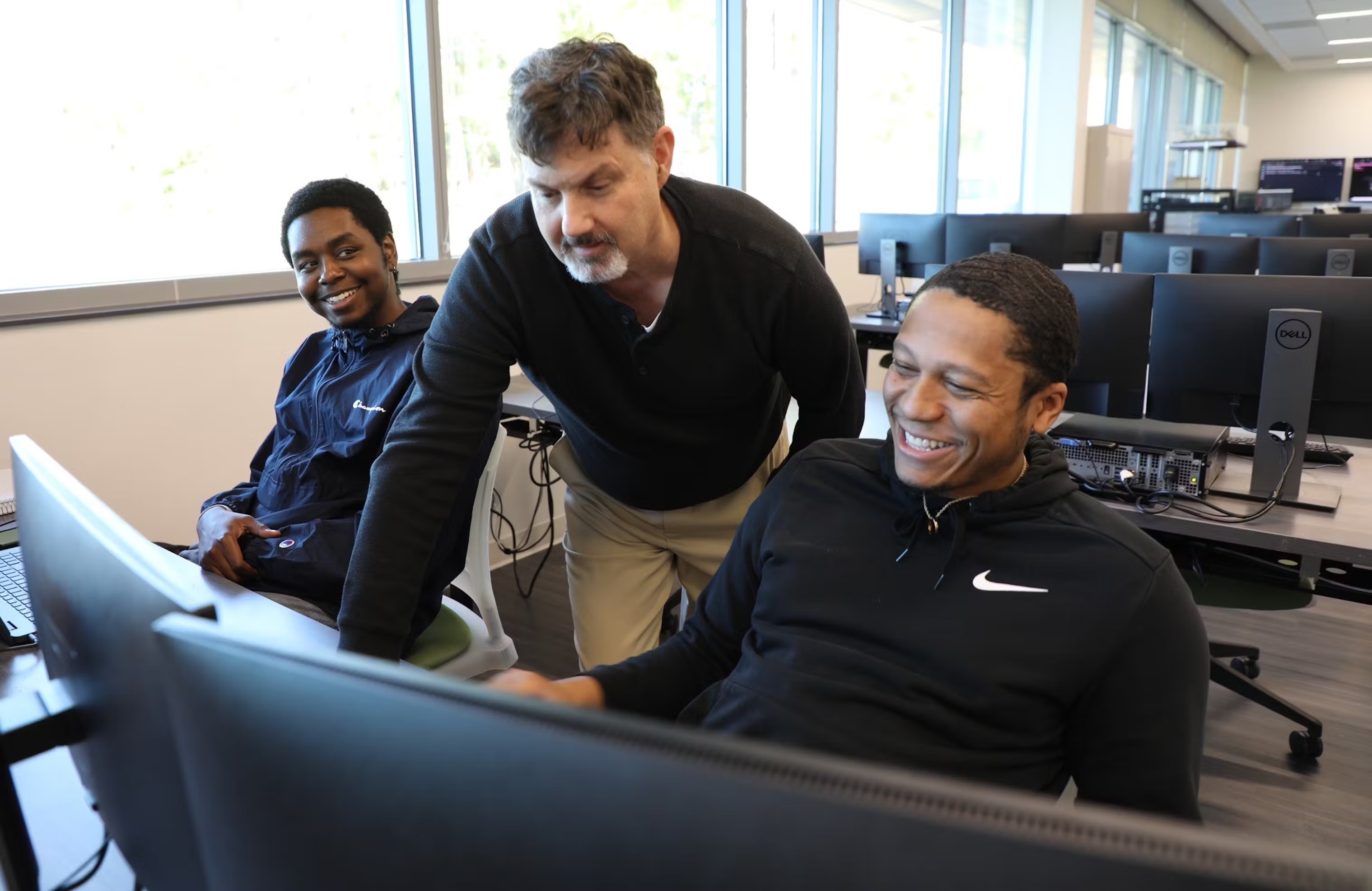 Instructor Scott Neal helping two students on a computer