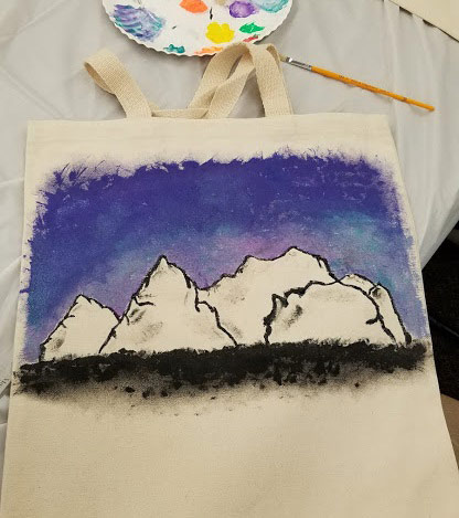 A mountain scene painted on a canvas tote bag