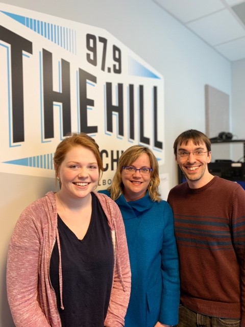 three people smiling in front of WCHL logo on wall