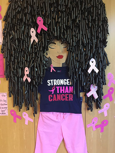 Image of woman wearing pink with a t-shirt reading Stronger than Cancer. She has large hairstyle with pink ribbons in it.