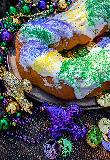 Ring of twisted cinnamon roll-style dough topped with icing or sugar, which may be colored to show the traditional Mardi Gras colors of green, yellow, and purple. Surrounded by beads.