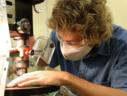 masked student carefully using a machining tool on a piece of metal