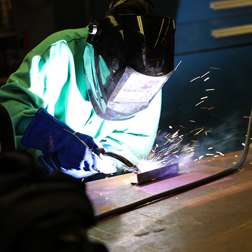 student wearing helmet using a welding torch 