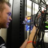 An Information Technology program student looks at a multi-colored server with LED lights as the student uses his hands to work on the server.